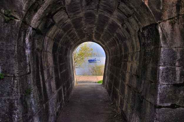 Visão geral de um túnel de tijolos em arco com vista para um lago com um barco na extremidade oposta