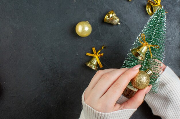 Visão horizontal da mão segurando a árvore de Natal e acessórios de decoração na mesa escura