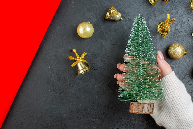 Visão horizontal da mão segurando os acessórios de decoração e a árvore de Natal em fundo escuro
