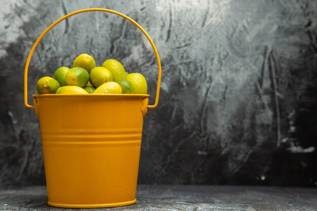 Visão horizontal de um balde amarelo cheio de tangerinas verdes frescas em fundo cinza