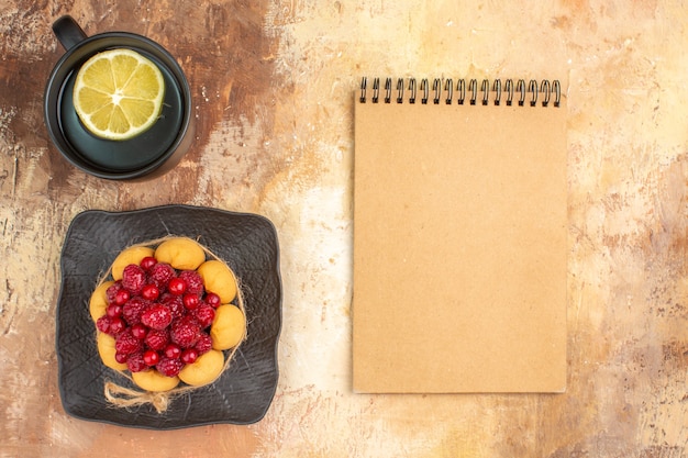 Visão horizontal de um bolo de presente com framboesas e uma xícara de chá com limão e caderno