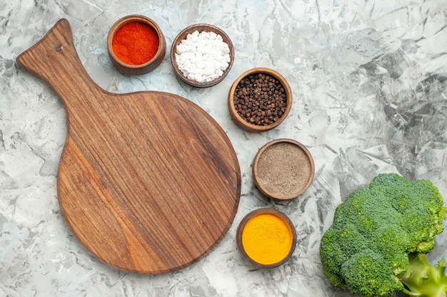 Visão horizontal de uma tábua de madeira saudável com diferentes especiarias e brócolis na mesa branca