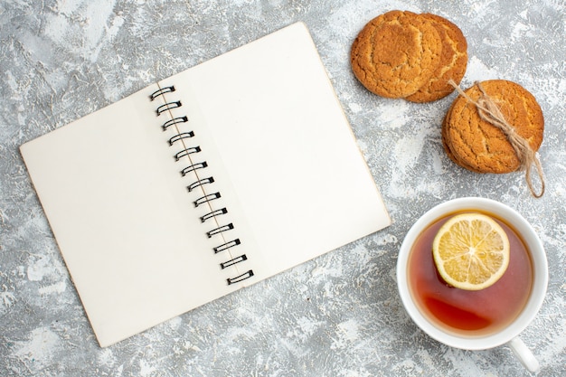 Visão horizontal de uma xícara de chá preto com limão e biscoitos deliciosos e o caderno aberto na superfície do gelo