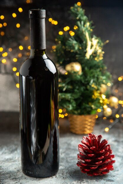 Visão vertical da árvore de natal atrás de uma garrafa de vinho vermelha para comemoração e um cone de conífera em fundo escuro