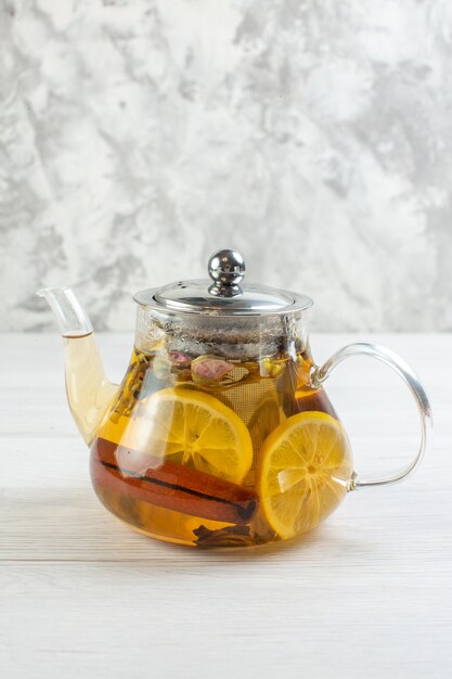 Visão vertical da hora do chá com chá de ervas misturado com limão em um pote de vidro na mesa branca