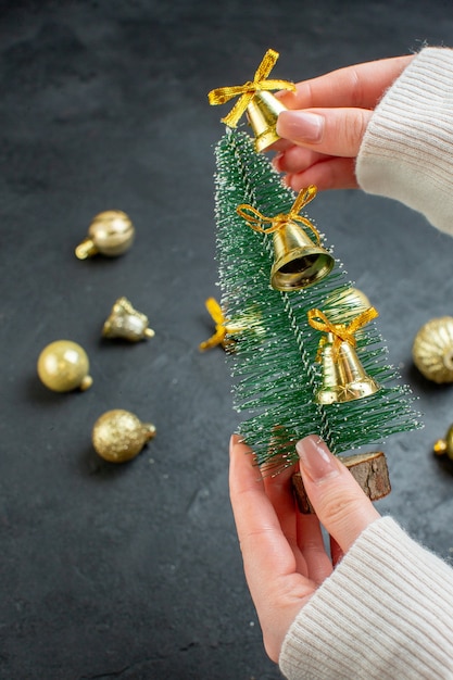 Visão vertical da mão segurando a árvore de Natal e acessórios de decoração em fundo escuro