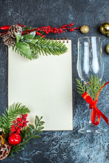 Visão vertical da taça de vidro caída com fita vermelha e acessórios de decoração ao lado do caderno em fundo escuro