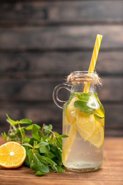 Visão vertical de água de desintoxicação servida com tubo de hortelã e laranja em um fundo marrom