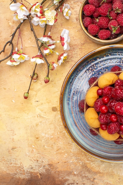 Visão vertical de bolo macio recém-assado com flores de frutas e biscoitos na mesa de cores misturadas