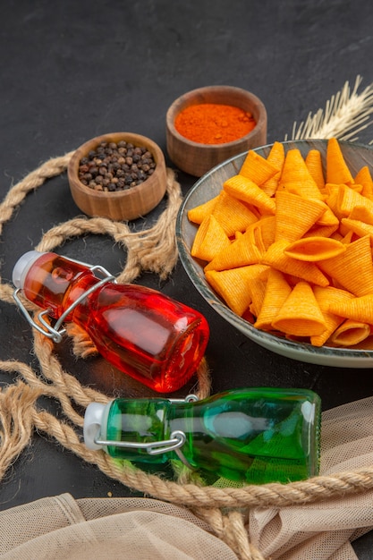 Visão vertical de deliciosas batatas fritas caídas de garrafas de pimentas na toalha e corda em um fundo preto