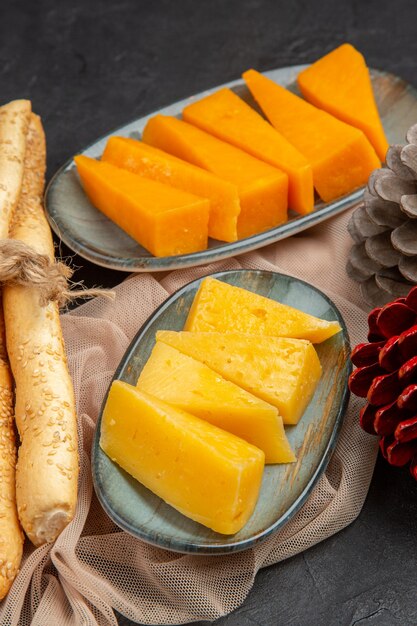 Visão vertical de deliciosas fatias de queijo e cones de coníferas em uma toalha em um fundo preto