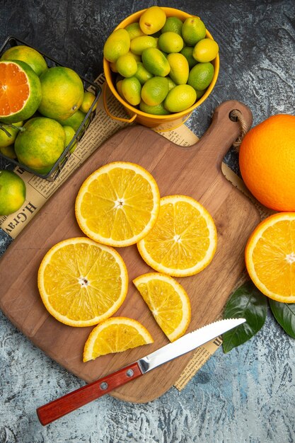 Visão vertical de frutas cítricas frescas com faca na tábua de madeira no jornal no fundo cinza