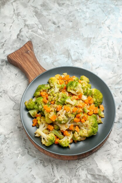 Visão vertical de salada de legumes fresca e saudável em uma tábua de madeira em fundo branco