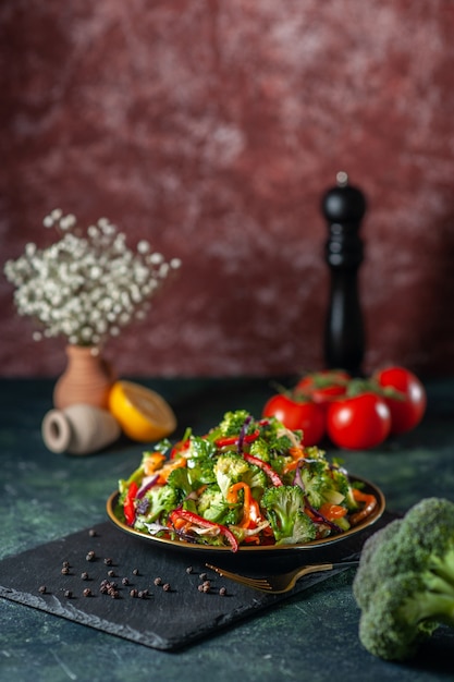 Visão vertical de salada vegana com ingredientes frescos em um prato e pimenta em uma tábua de corte preta