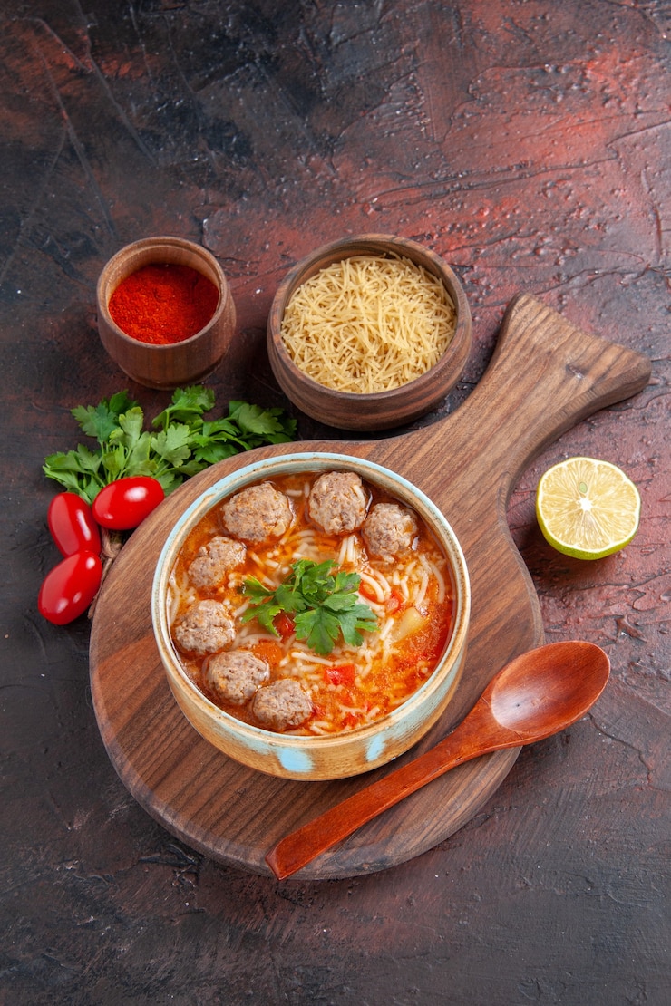 Foto grátis visão vertical de sopa de almôndegas de tomate com macarrão em uma tigela marrom e especiarias diferentes em fundo escuro