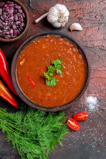 Visão vertical de sopa de tomate em uma tigela marrom e diferentes especiarias, alho e limão na mesa de cores diferentes