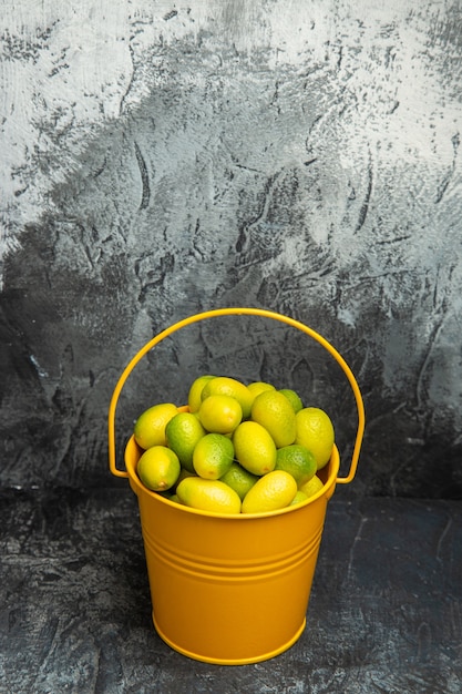 Visão vertical de um balde amarelo cheio de tangerinas verdes frescas em fundo cinza