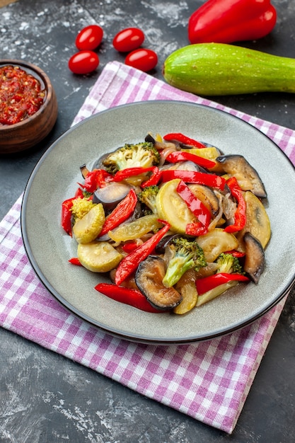 Visão vertical de uma deliciosa refeição sem carne em um prato na toalha roxa despojada e molho de vegetais em fundo escuro