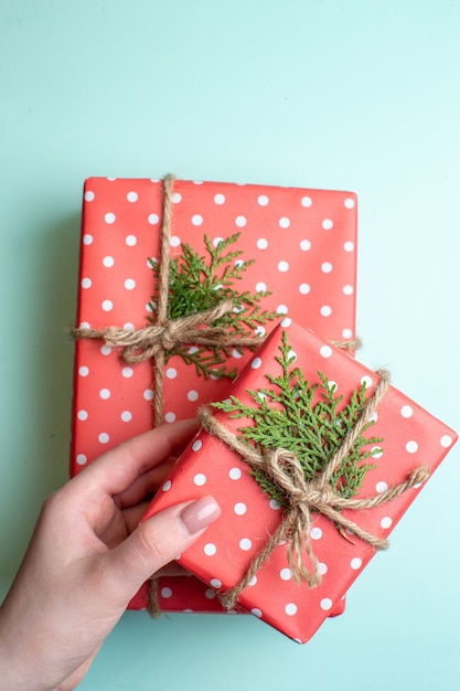 Visão vertical do plano de fundo do Natal com a mão segurando caixas de presente vermelhas sobre fundo verde pastel