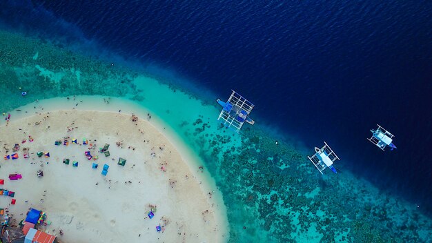 Vista aérea da praia de areia com turistas que nadam na linda água do mar clara da ilha de Sumilon, pousando na praia perto de Oslob, Cebu, Filipinas. - Impulse o processamento de cores.