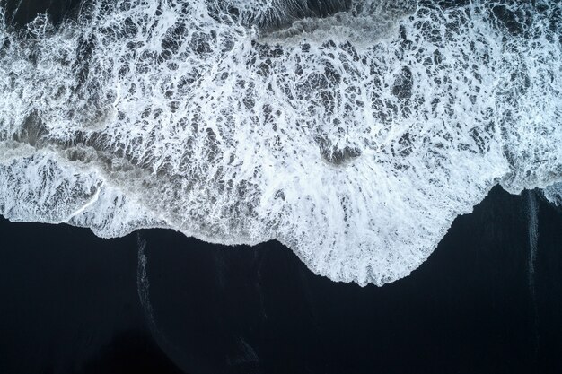 Vista aérea da praia de areia preta e das ondas do mar na Islândia.