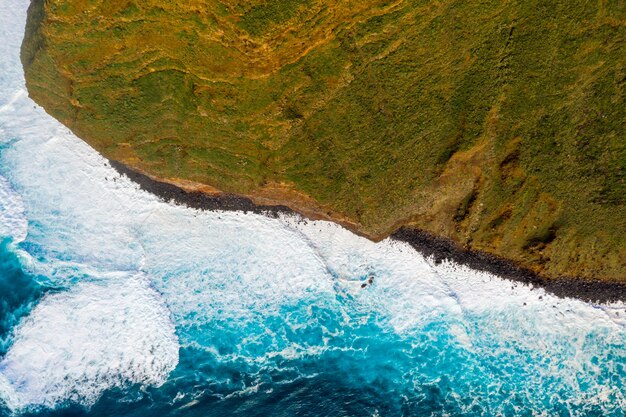Vista aérea das falésias da ilha do oceano com enormes ondas brancas e água azul cristalina