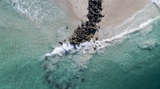 Vista aérea das ondas do mar quebrando pela pilha de pedras na praia