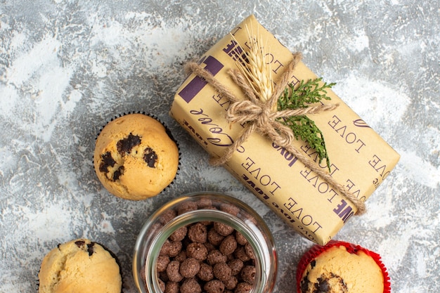 Foto grátis vista aérea de deliciosos bolinhos pequenos e chocolate em uma panela de vidro ao lado do presente de natal na superfície do gelo