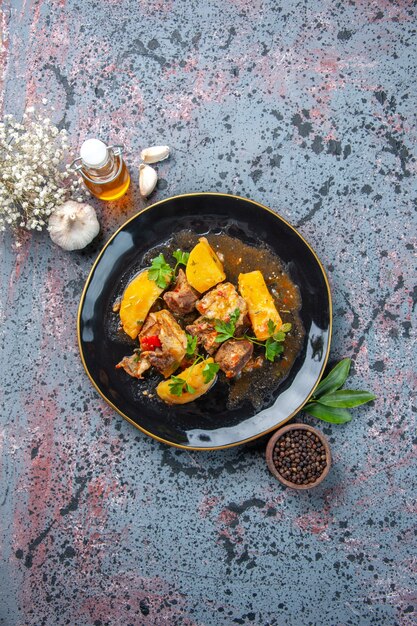 Vista aérea de um delicioso jantar com batatas de carne servidas com verde em um prato preto e garrafa de óleo de alho com pimenta