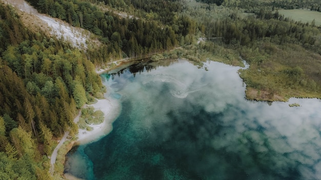 Vista aérea de um lago cercado por florestas com o céu nublado refletindo na água