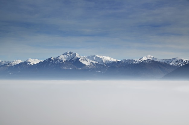 Vista aérea incrível de montanhas parcialmente cobertas de neve e posicionadas acima das nuvens