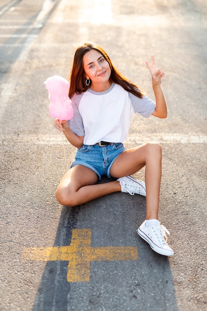 Vista alta mulher sentada na estrada comendo algodão doce