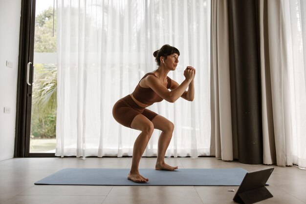 Vista aproximada de uma jovem desportista sorridente fazendo exercício em casa no laptop no karamet