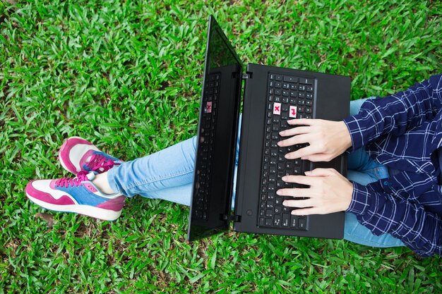 Vista colhida da menina trabalhando no laptop na grama