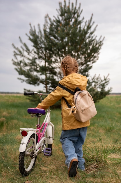 Vista da menina com mochila e bicicleta aventurando-se na natureza