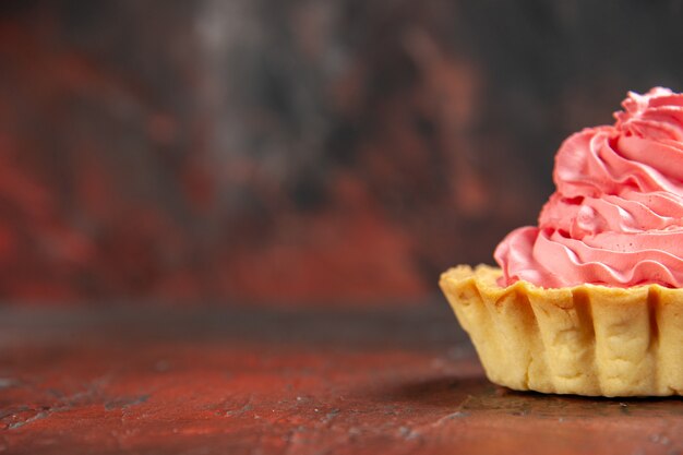 Vista da metade frontal pequena torta com creme de confeiteiro rosa no espaço livre da mesa vermelho escuro