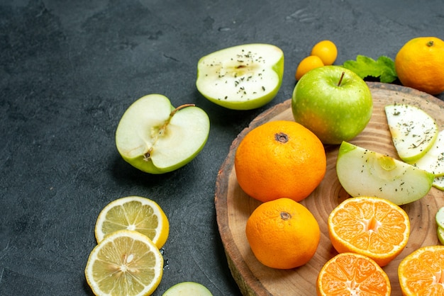 Vista da metade inferior corte maçãs e tangerinas em uma tábua de servir rústica corte rodelas de limão na mesa escura