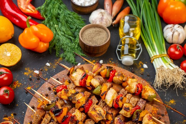 Vista da metade inferior espetos de frango assado com crosta na placa de madeira e outros alimentos na mesa