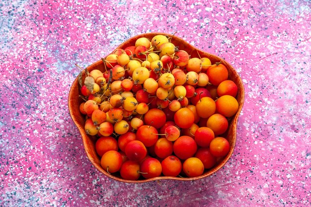 Vista da metade superior cerejas doces frescas com ameixas dentro do prato na mesa rosa.