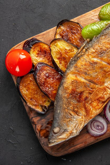 Vista da metade superior peixe frito berinjela frita cebola na tábua de servir de madeira na superfície escura