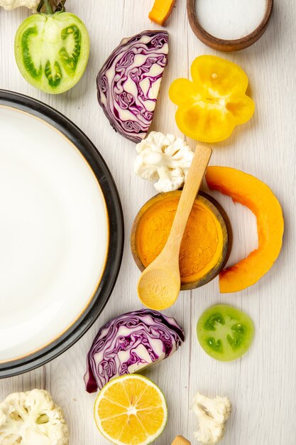 Vista da metade superior prato branco corte legumes repolho vermelho abóbora couve-flor açafrão amarelo pimentão em uma tigela pequena na superfície de madeira branca