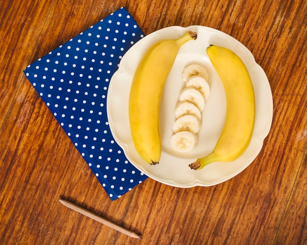 Foto grátis vista de alto ângulo de bananas; lápis e caderno na mesa de madeira