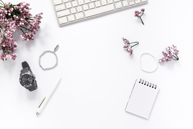 Vista de alto ângulo de flor; pulseira; relógio de pulso; caneta; bloco de notas em espiral; e teclado no fundo branco