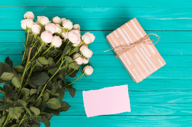 Vista de alto ângulo de rosas brancas; caixa de presente e papel em branco sobre o pano de fundo verde