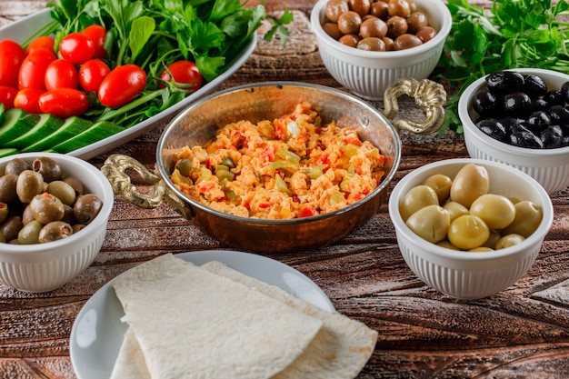 Vista de alto ângulo deliciosa refeição em panela com salada, picles em tigelas na superfície de madeira