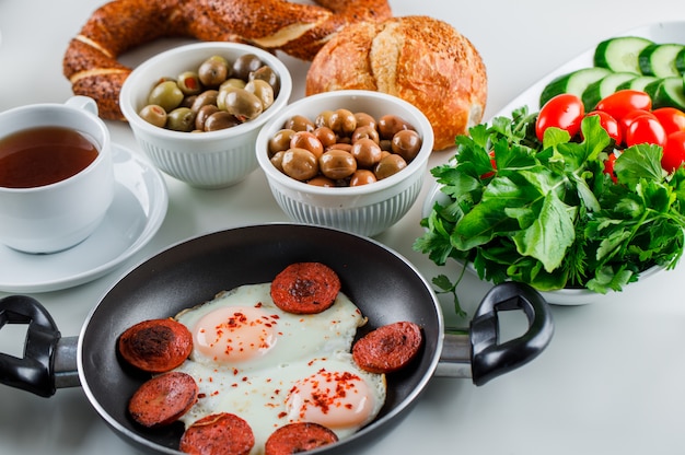 Vista de alto ângulo, deliciosas refeições em panela com uma xícara de chá, pão turco, tomate, verduras na superfície branca