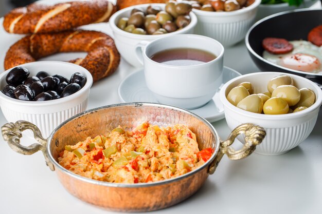 Vista de alto ângulo, deliciosas refeições em panela com uma xícara de chá, pão turco, tomate, verduras na superfície branca