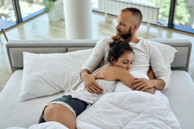 Vista de alto ângulo do jovem casal apaixonado abraçando enquanto estava deitado na cama