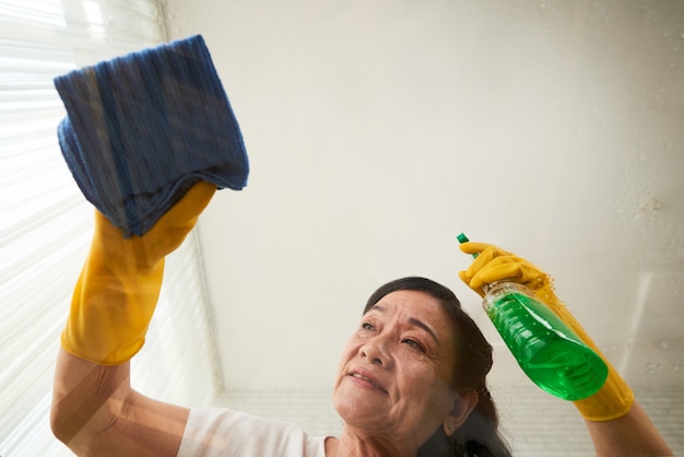 Foto grátis vista de ângulo baixo da mulher sênior, limpando a mesa de vidro com spray