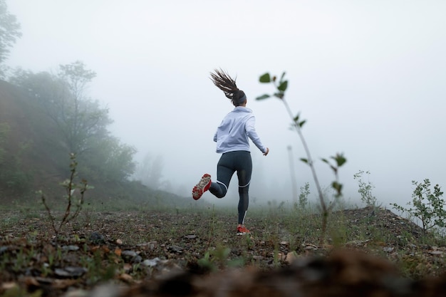 Vista de ângulo baixo de desportista motivada correndo na natureza durante o tempo enevoado Copiar espaço